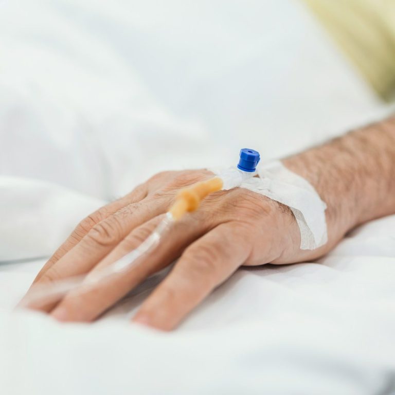 A person's hand with an intravenous line attached, resting on a hospital bed.