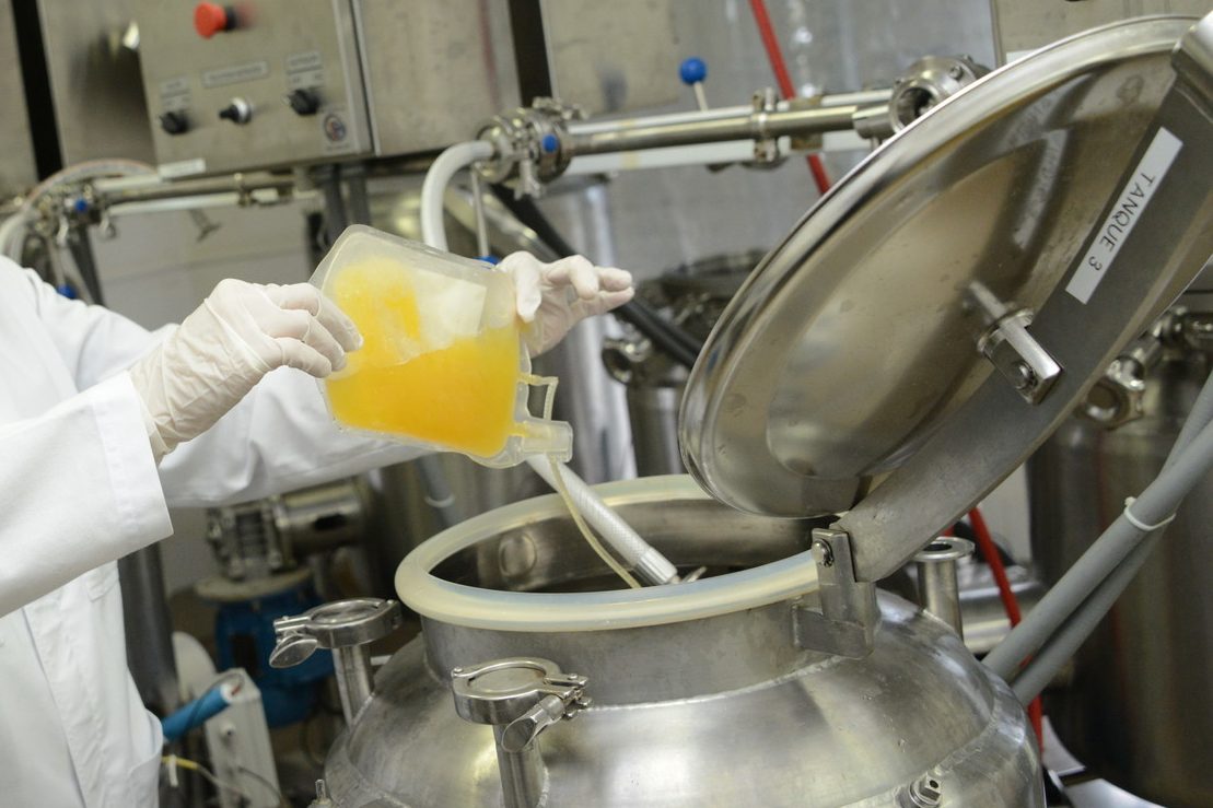 A production worker pours yellow plasma into a large stainless steel container.